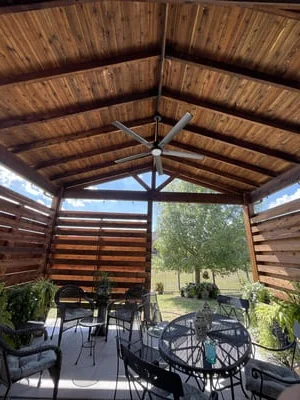 Wooden pavilion with exposed beams, louvered siding, and concrete patio with outdoor furniture
