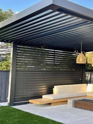 Modern pergola with adjustable louvers and privacy screen over concrete patio with seating area
