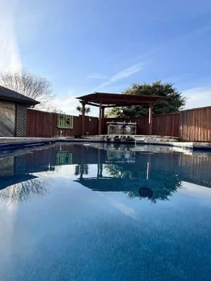 Rectangular pool with pergola structure, wooden fence, and mature landscaping