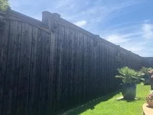 Tall vertical board fence with dark finish installed along residential property with green lawn