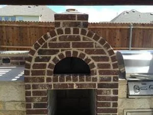 Arched brick pizza oven with detailed masonry dome and dark interior opening in backyard setting