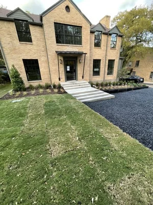 Asphalt driveway with concrete steps, new sod lawn, and landscape beds at brick home entrance