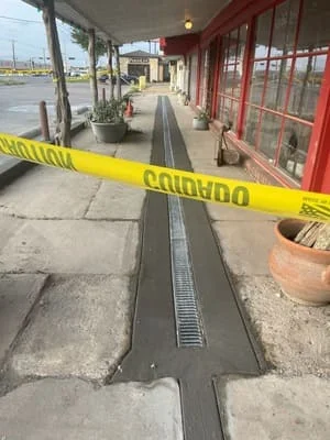 Linear metal grate drainage channel installed in concrete walkway along commercial storefront