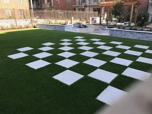 Checkerboard pattern of green synthetic turf and white pavers in outdoor space