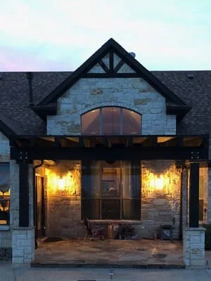 Tudor pavilion with timber framing, blue stone veneer, and concrete patio at dusk