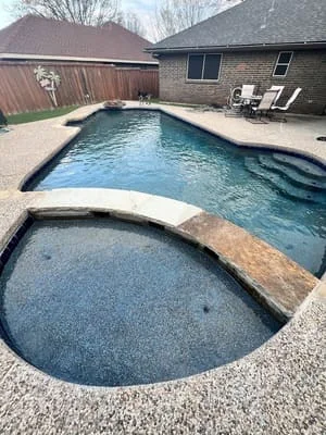 Rectangular pool with attached spa, concrete decking, and brick home backdrop