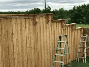 Vertical wood privacy fence with stepped sections and aluminum ladders during installation