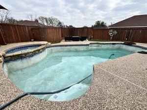 Custom pool with spa, concrete deck, and wooden fence in residential backyard