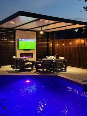 Modern patio with pergola, LED-lit pool, seating, and landscape lighting at dusk
