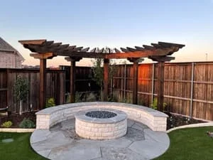Circular stone fire pit with seating wall on stamped concrete patio, wooden pergola overhead