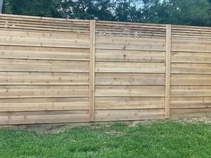 Horizontal wood privacy fence with pressure-treated boards and post construction against green lawn