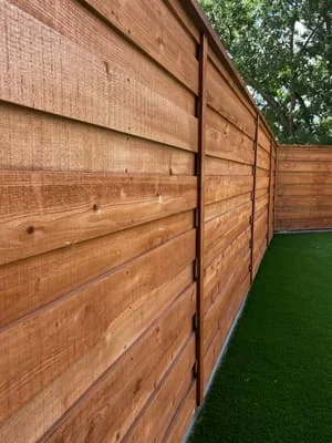 Horizontal cedar wood fence with metal posts and brackets installed next to artificial turf lawn