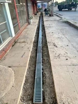 Linear drainage trench with metal grate cover installed along commercial storefront sidewalk