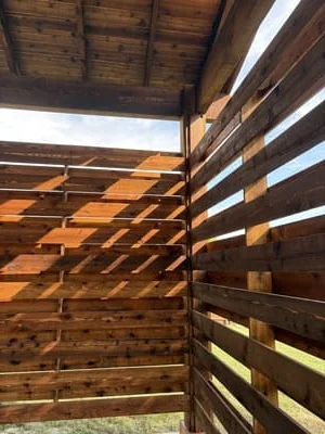 Wooden pergola with horizontal slats and metal beam supports creating filtered shade