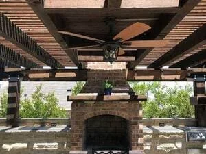 Brick fireplace with pergola, wood ceiling, and potted plants in outdoor patio