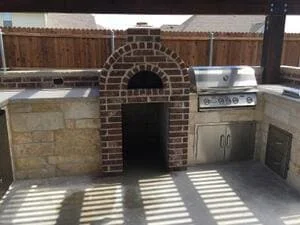 Brick pizza oven with arched entrance, built-in grill, and concrete countertops in outdoor kitchen