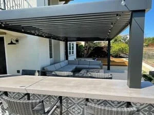 Motorized louvered pergola over concrete patio with built-in outdoor kitchen and stainless steel grill