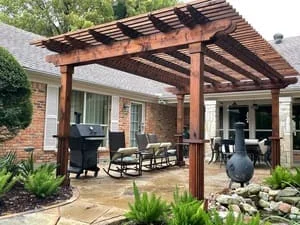 Stained timber pergola over patio with landscape beds and ornamental plantings