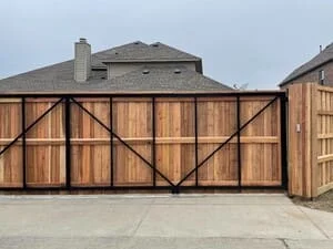 Wooden driveway gate with board-and-batten panels and black X-bracing over concrete apron