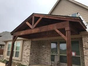 Timber frame patio cover with exposed beams attached to brick home