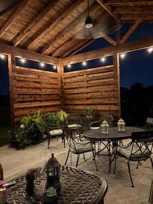 Wooden pavilion with beam ceiling, string lights, and outdoor dining setup on concrete patio