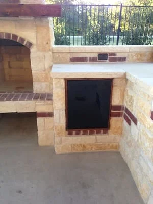 Stacked stone outdoor kitchen with arched fireplace opening and brick accents