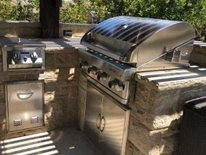 Built-in stainless steel grill and refrigerator in stone veneer outdoor kitchen