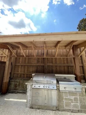 Wooden pergola structure with exposed beams sheltering outdoor grill and kitchen appliances